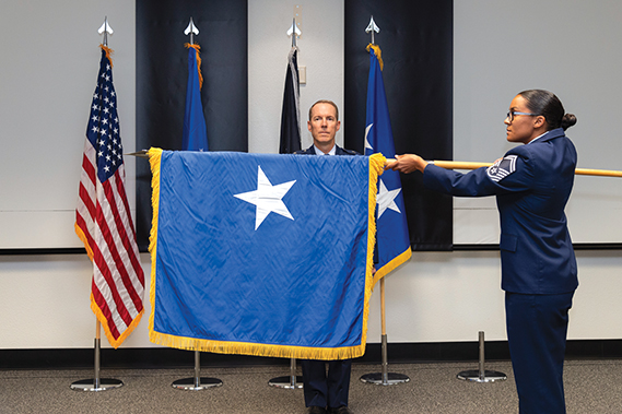 SMSgt Tanya Sipos unfurls the new flag for Brigadier General Douglas P. Wickert, Commander, Edwards Air Force Base. The Air Force Test Center, the 412th Test Wing, family, friends, and other distinguished guests gather to celebrate the promotion of the Commander.